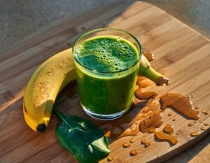 כוס שייק ירוק על רקע אור בוקר רך, ליד בננה ועלה תרד. טיפות מים על הכוס מרמזות על רעננות.